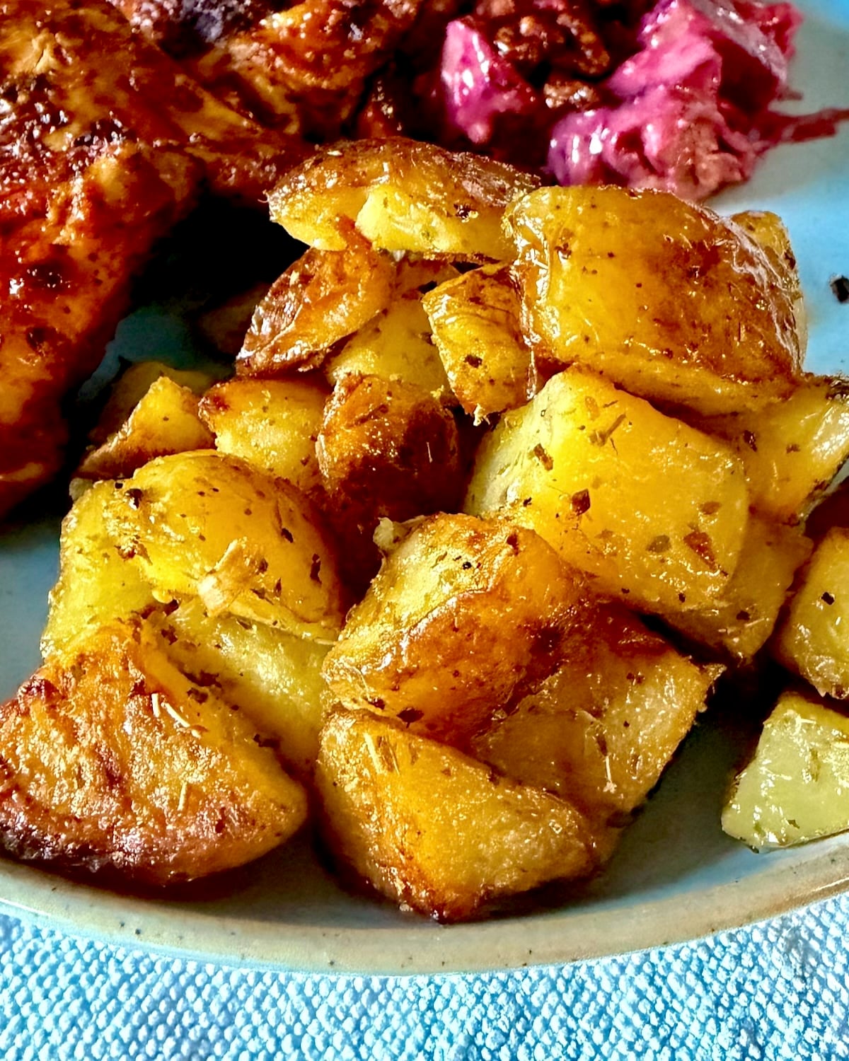 Lemon Oregano Oven Potatoes pictured with peri peri chicken on a blue plate.