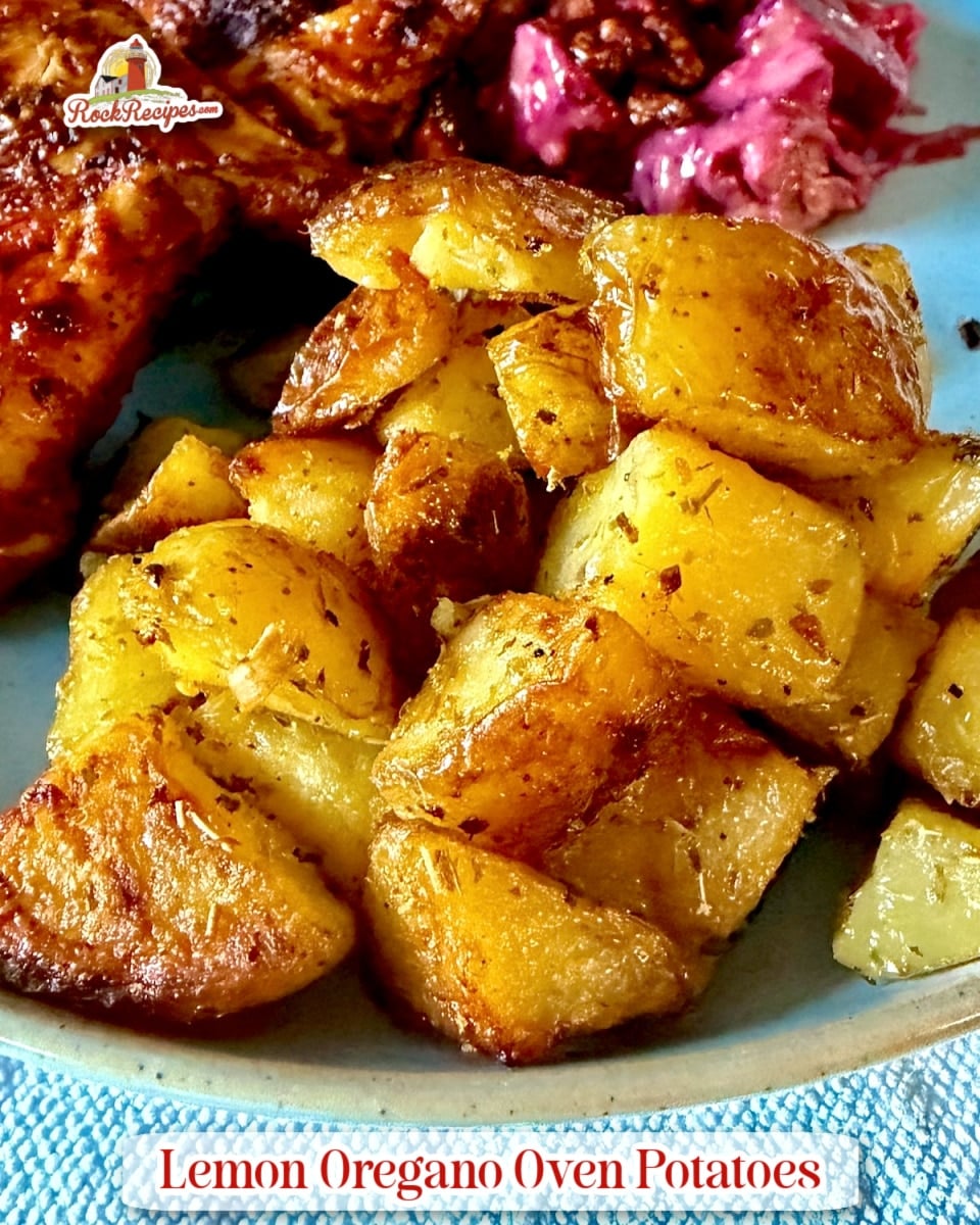 Lemon Oregano Oven Potatoes pictured with peri peri chicken on a blue plate with title text added for Pinterest and social media posts.