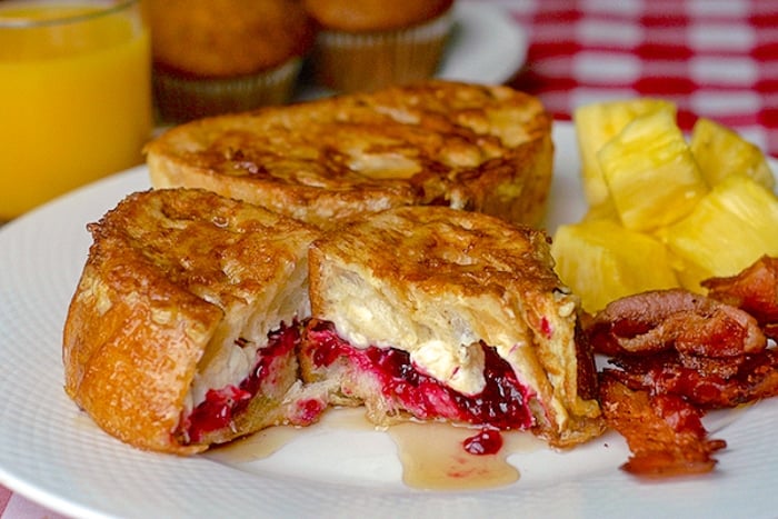 Partridgeberry Cream Cheese Stuffed French Toast on a white plate with bacon and fruit