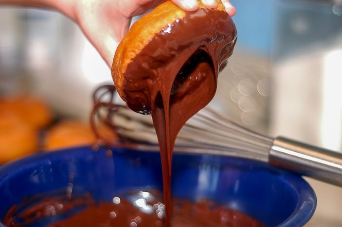 Homemade donuts being dipped in chocolate glaze