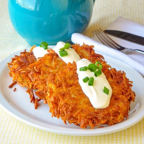 Garlic Parmesan Potato Latkes shown on a white plate with a dollop of sour cream