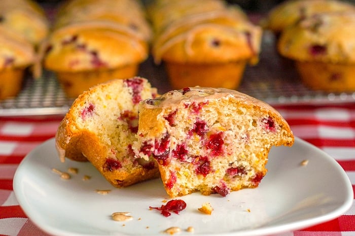 Cranberry Orange Muffins wide shot of muffins in background single muffin in foreground on white plate.