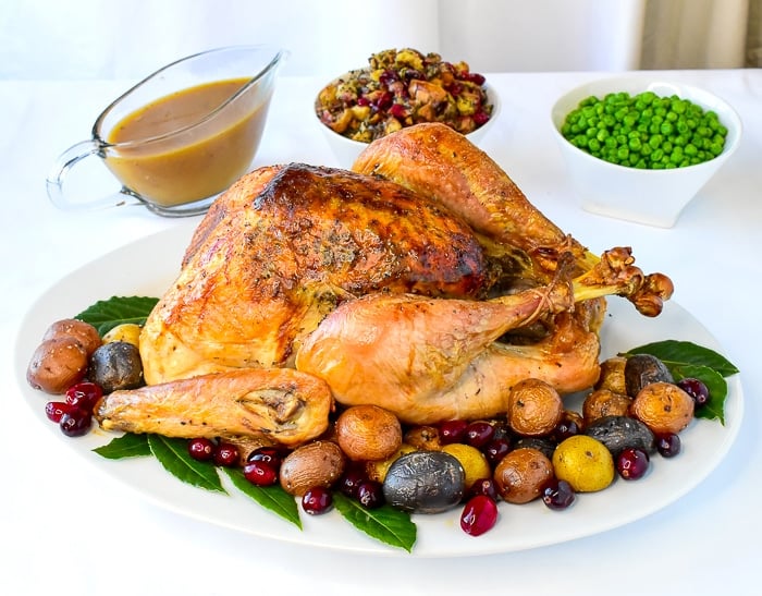 Overhead photo of finished turkey on a white platter with herb cranberry stuffing, gravy and peas