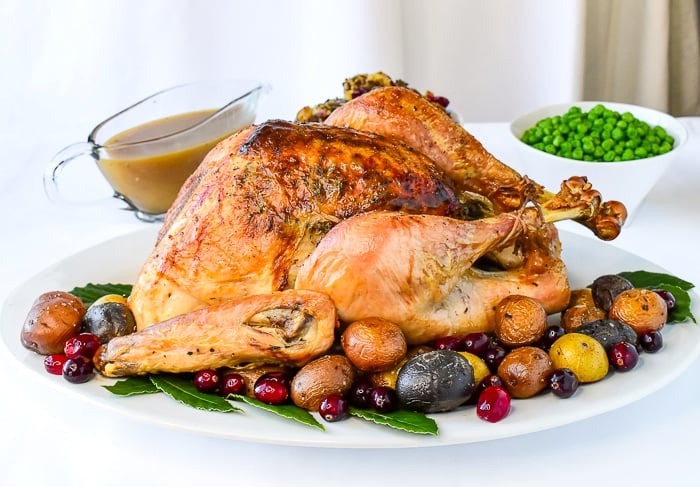 Turkey on a white platter surrounded by roasted potatoes and cranberries