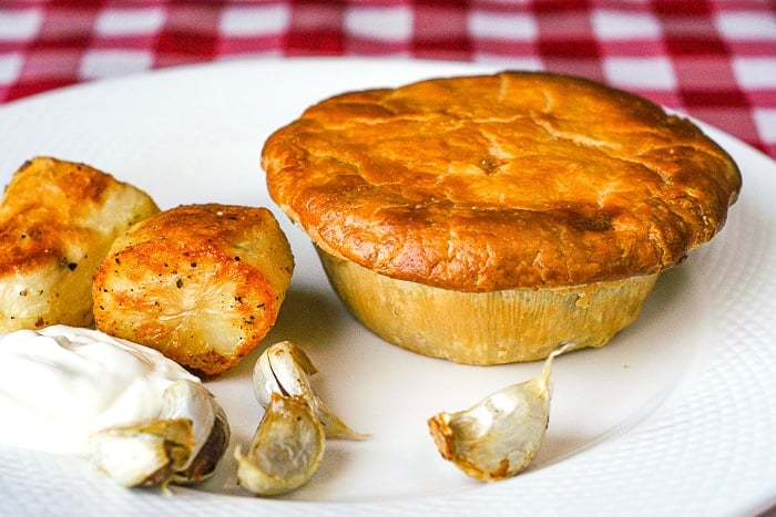 Turkey Pot Pie uncut on a white plate with roasted potatoes and sour cream.