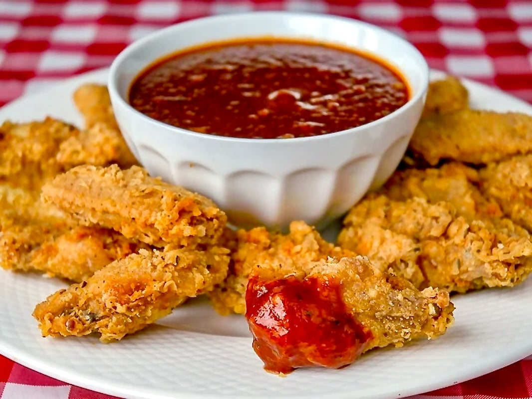 Wide shot photo of fried chicken wings on a white platter with bowl of BBQ sauce in the cente.