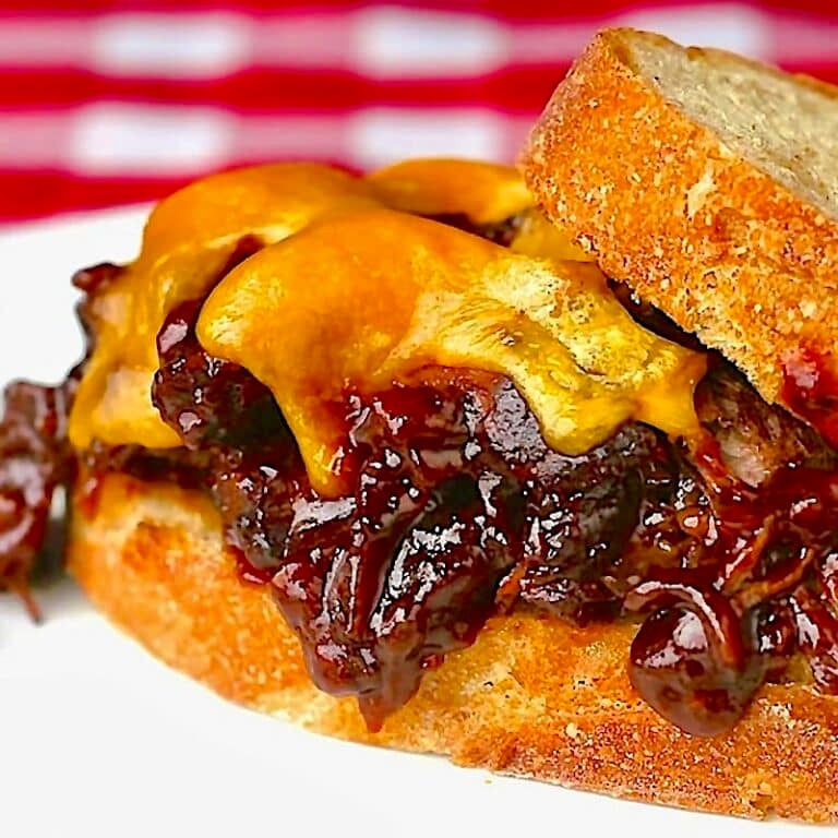 Molasses Barbecue Braised Beef Sandwiches close up photo of one sandwich with melting cheddar cheese.