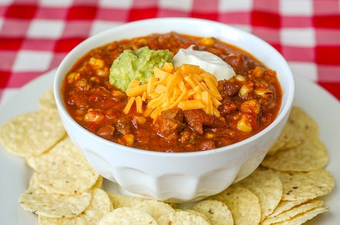 Grilled Corn Sausage Chili pictured in a white bowl surrounded by tortilla chips.