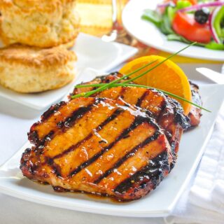 Orange Glazed Pork Chops with Cardamom and Honey close up photo of grilled and glazed chops on a white platter