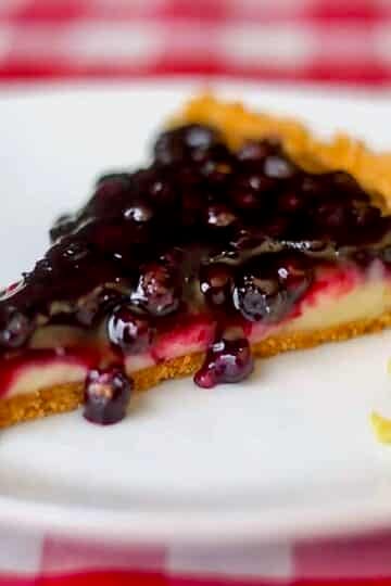 Photo of a single slice of Lemon Blueberry Tart on a white plate.