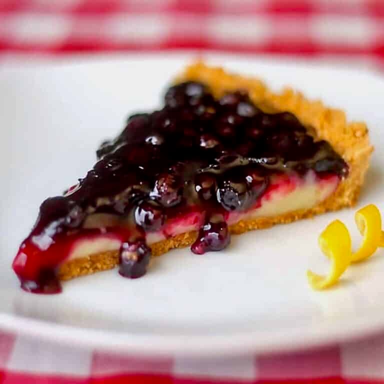 Photo of a single slice of Lemon Blueberry Tart on a white plate.