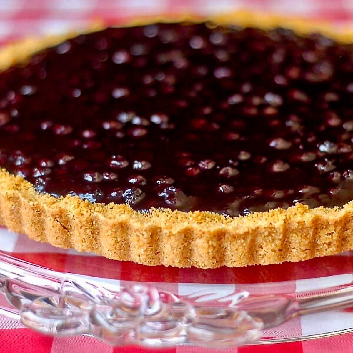 Close Up Photo of an uncut Lemon Blueberry Tart on a clear glass rose embossed cake plate.