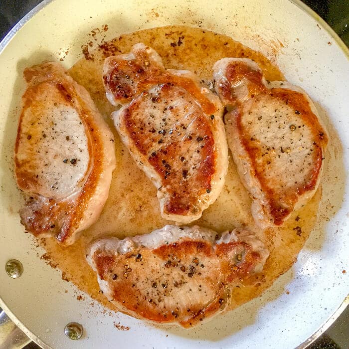 Honey Ginger Dijon Glazed Pork Chops. a simple pan seared method. shown in skillet as they are cooking.