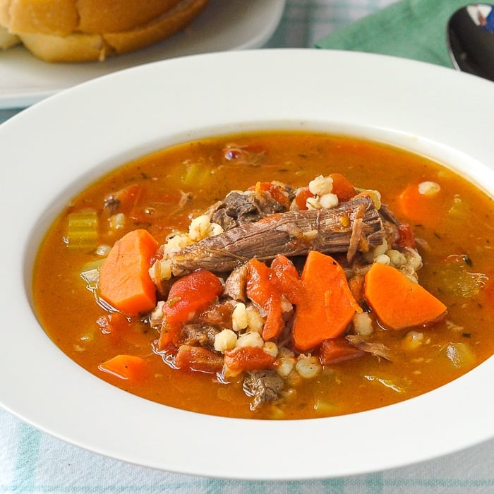 Beef Barley Soup with Tomatoes close up photo pf soup in a white bowl.