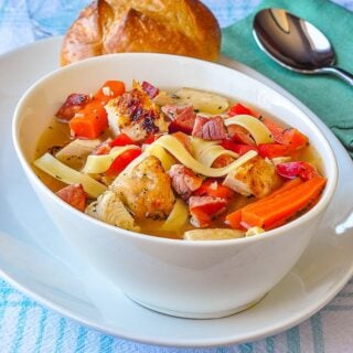 Chorizo Rotisserie Chicken Noodle Soup photo of a singe serving in white bowll with a bread roll on the side