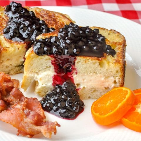 Cream Cheese Stuffed French Toast with Blueberry Sauce shown with bacon and orange slices on a white plate