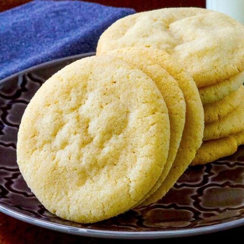 Soft and Chewy Sugar Cookies stacked on a grey patterned plate with a glass of milk in the background