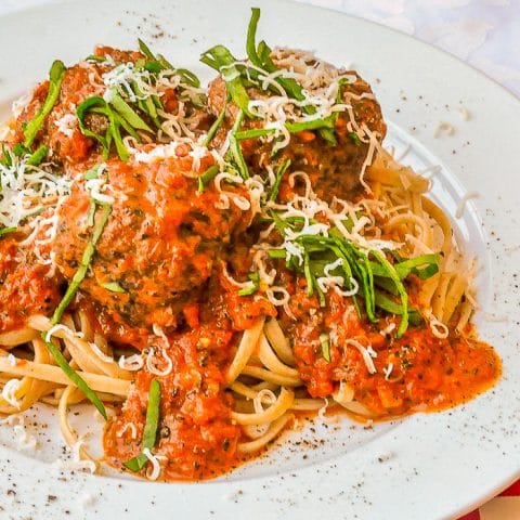 Linguine with Meatballs in Blush Asiago Sauce shown on a white plate with basil and grated cheese garnish