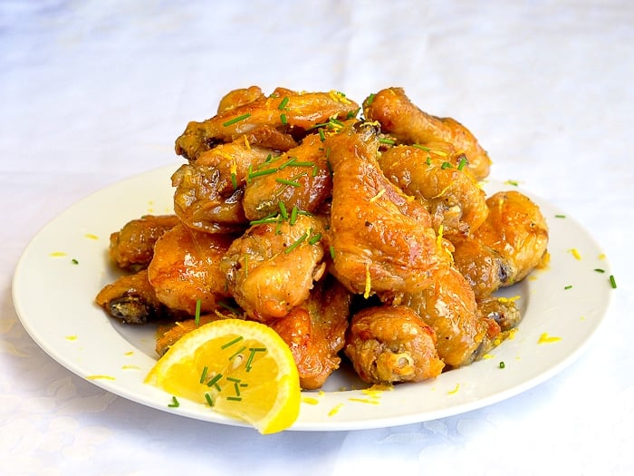 Baked Honey Lemon Glazed Wings stacked on a white plate with lemon and chive garnish