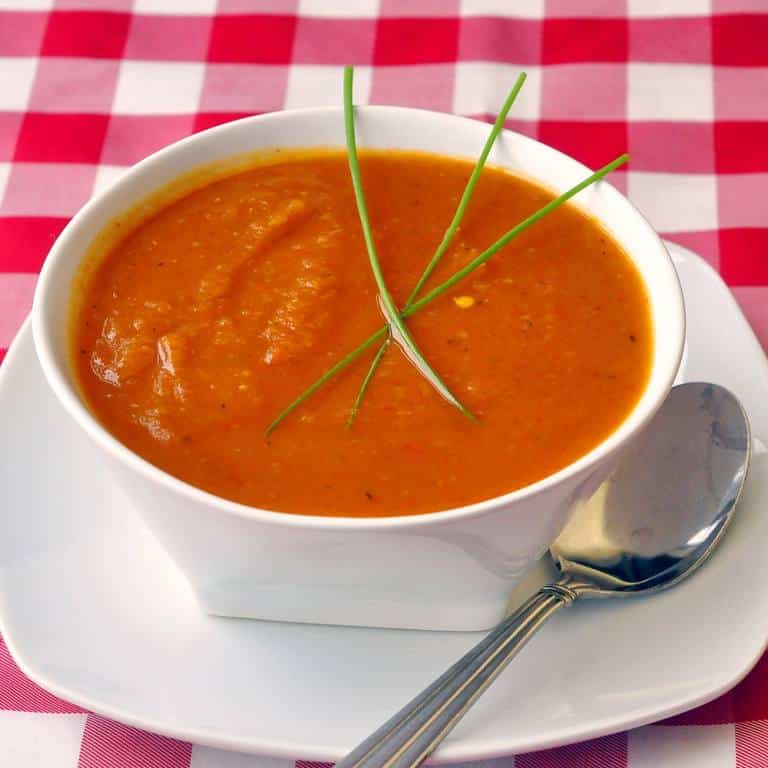 Roasted Squash and Red Pepper Soup in a white bowl with checkered tablecloth.
