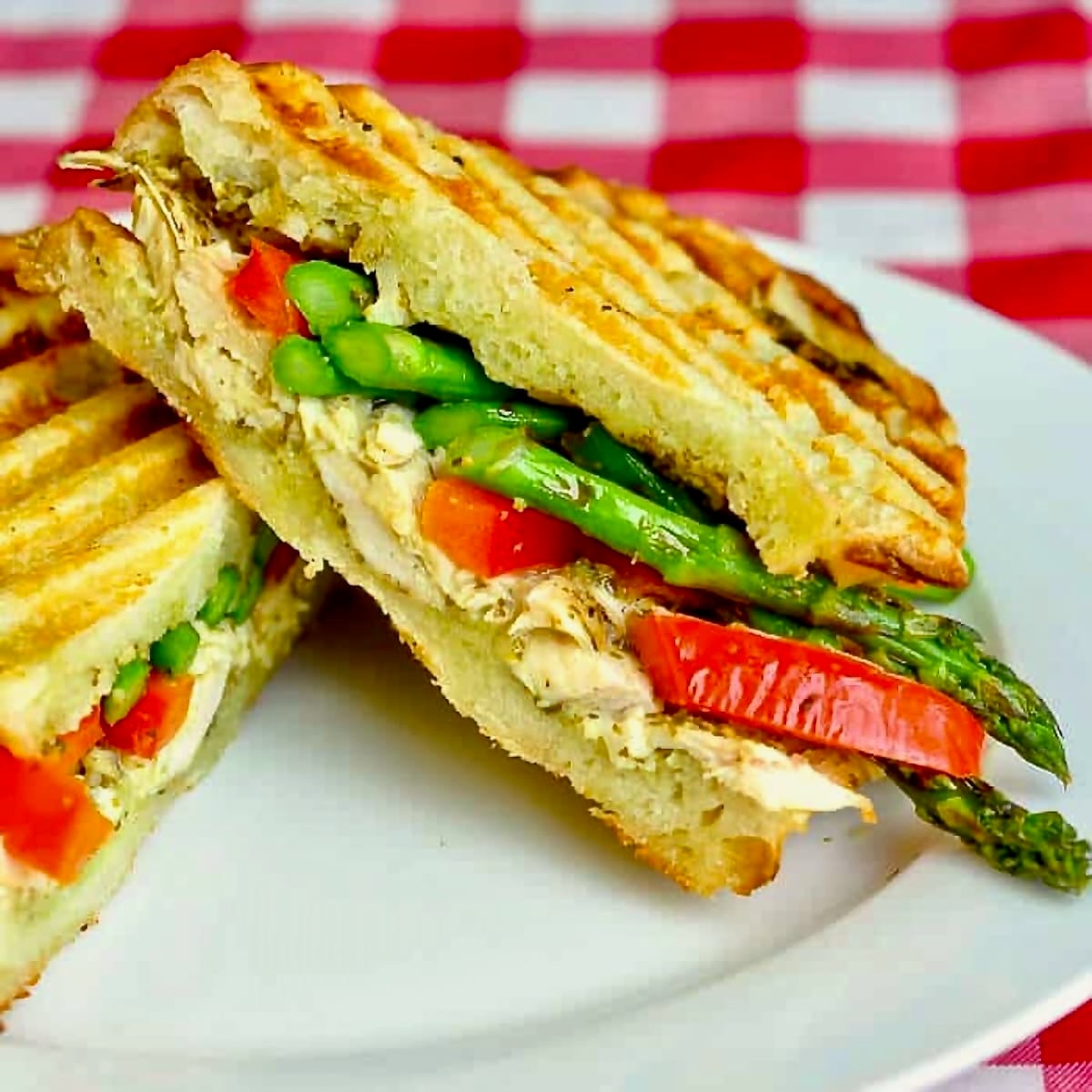 Photo of Asparagus Panini with pesto and grilled chicken shown on a white plate.