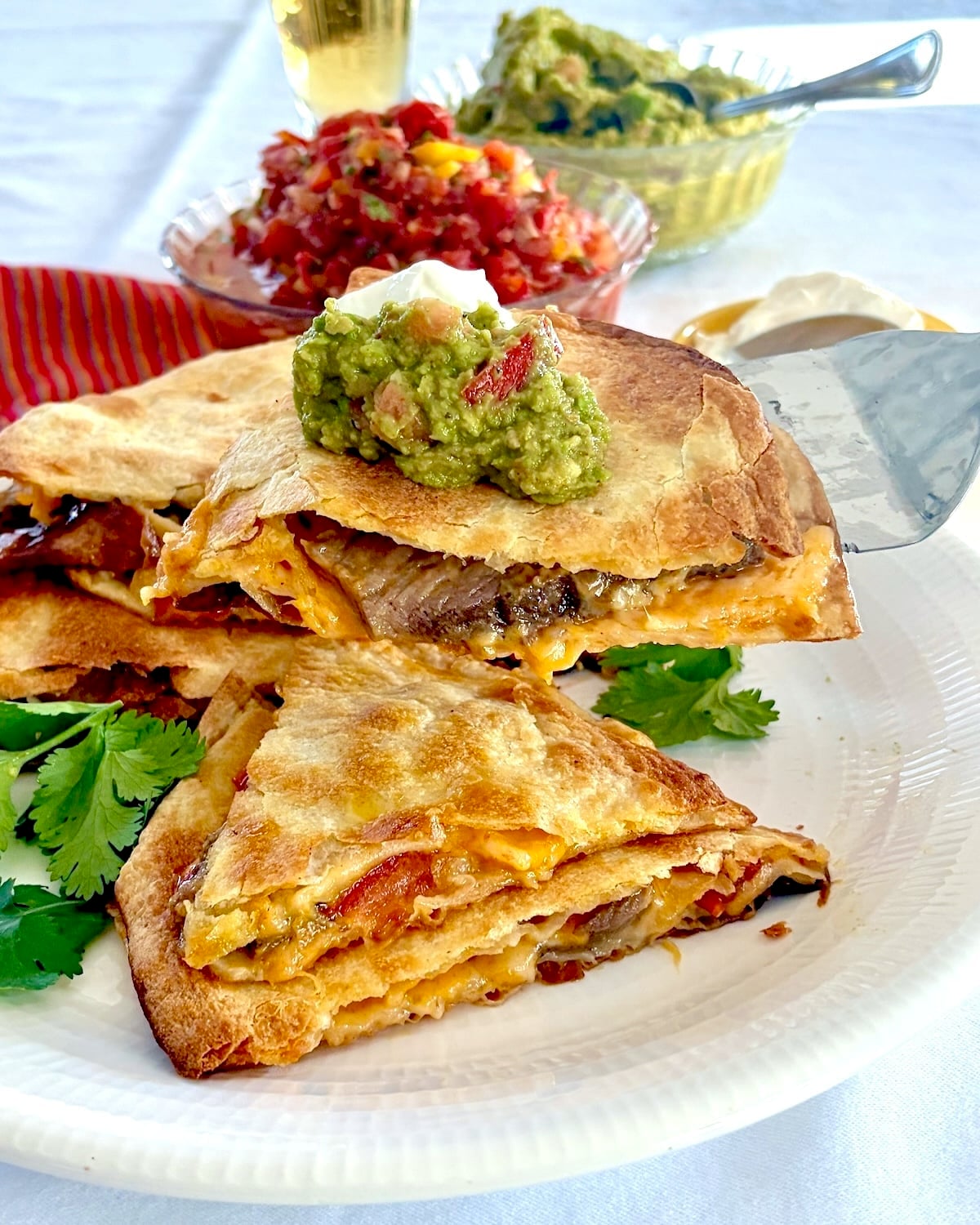 No Fry Oven Quesadillas. with guacamole and sour cream and salsa in the background.