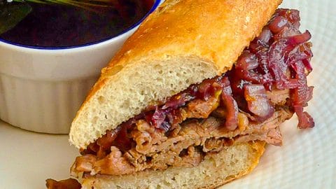 French Dip Sandwich close up photo of a sandwich cut on a white plate with dip in a ramekin on the plate.