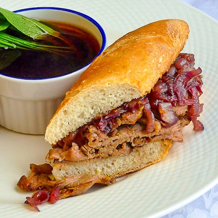 French Dip Sandwich close up photo of a sandwich cut on a white plate with dip in a ramekin on the plate.