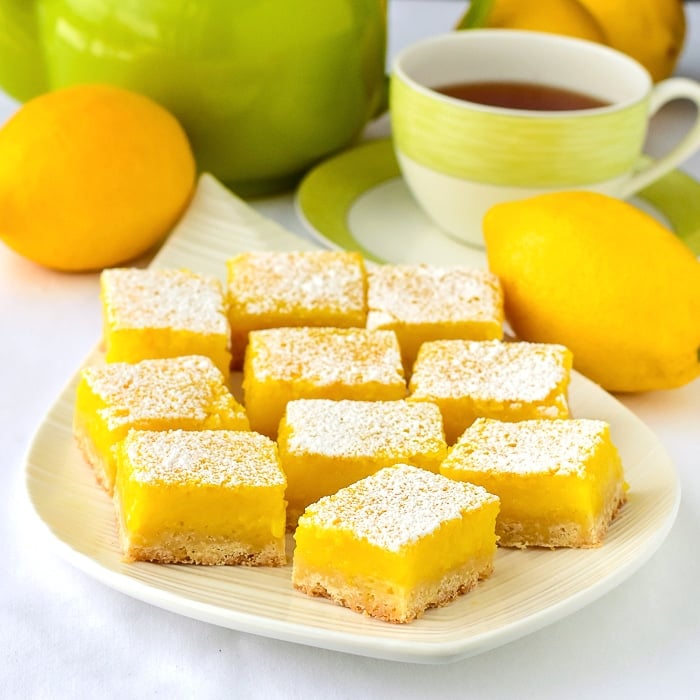 Lemon bars on a white platter with tea service in the background