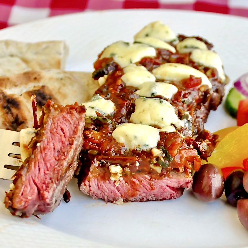 Blue Cheese Streak Puttanesca on a white plate with salad and flatbread