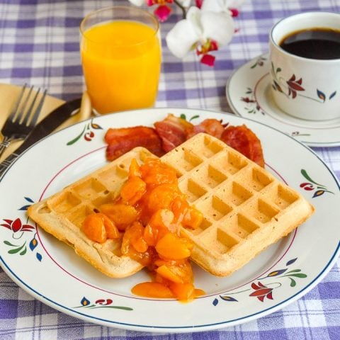 Cinnamon Waffles with Apricot Orange and Brandy Compote shown on flower pattern plate with orange juice and coffee in background
