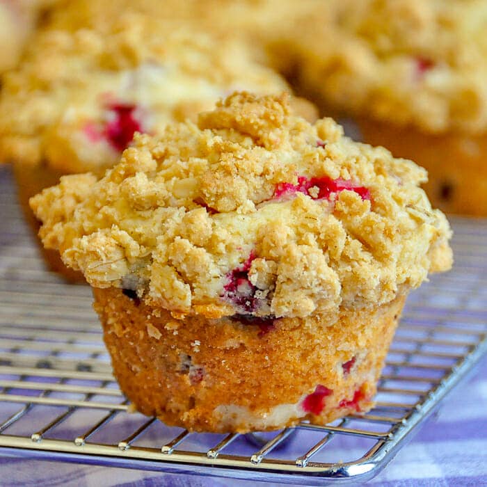 Cranberry Crunch Muffins. single muffin with muffins on cooling rack in background.