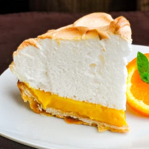 Orange Curd Meringue Tart photo of a single slice on a white plate with orange slice and mint garnish