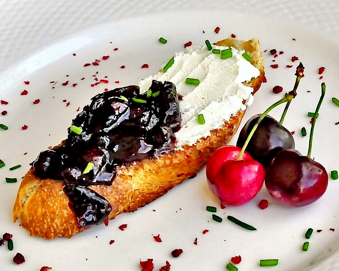 Goat Cheese Bruschetta with Roasted Cherry & Pink Peppercorn Jam. shown on a white plate.
