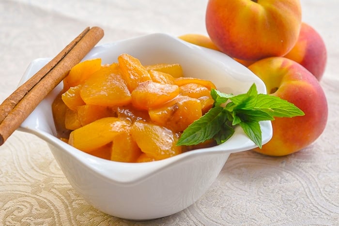 Honey Peach Compote in a white bowl with fresh peaches in background