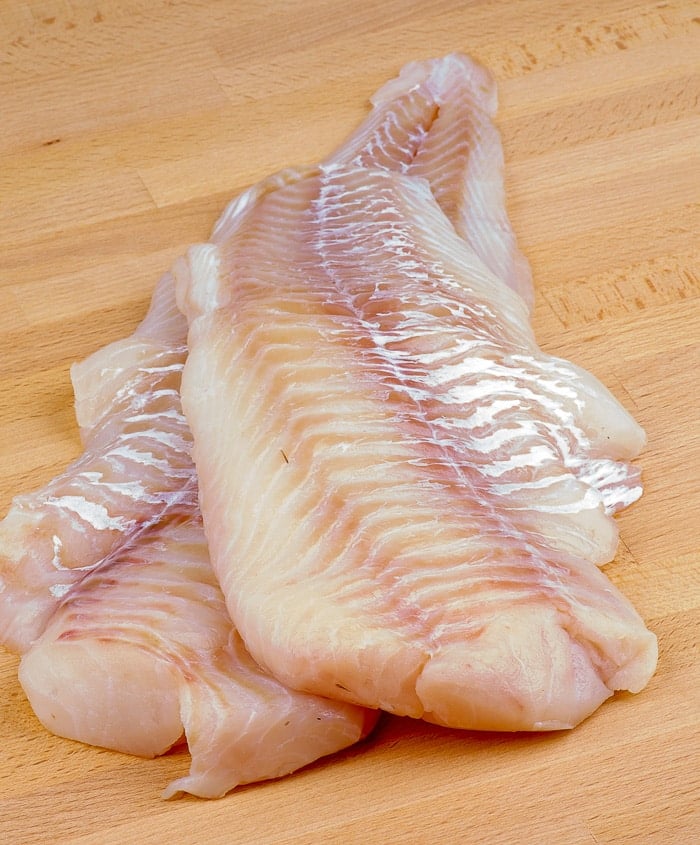 Two Slices of Raw Fresh Cod Fish Fillet closeup on Wooden Cutting Board