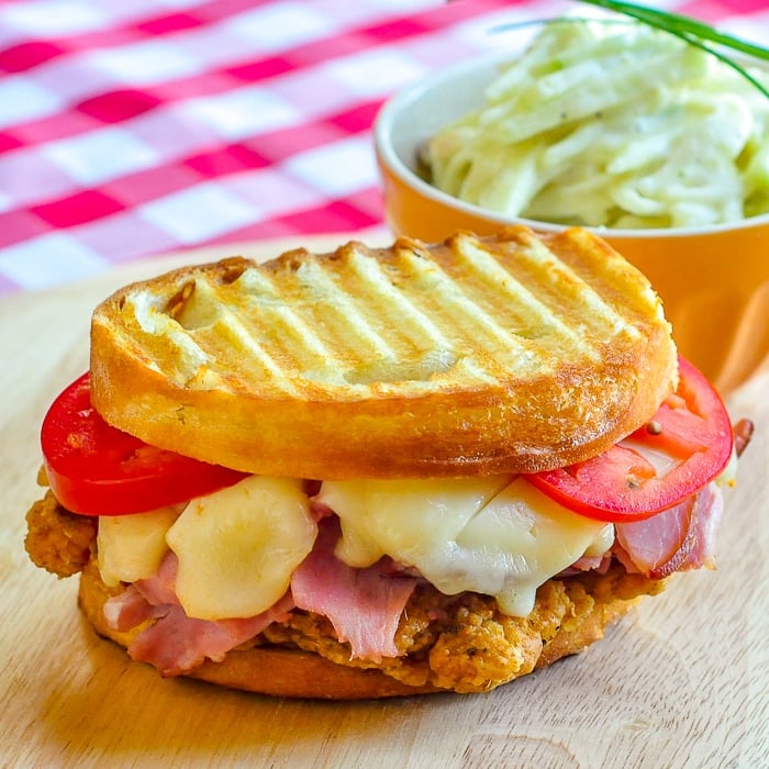 Fried Chicken Club Sandwich Panini pn a wooden cutting board with coleslaw in background