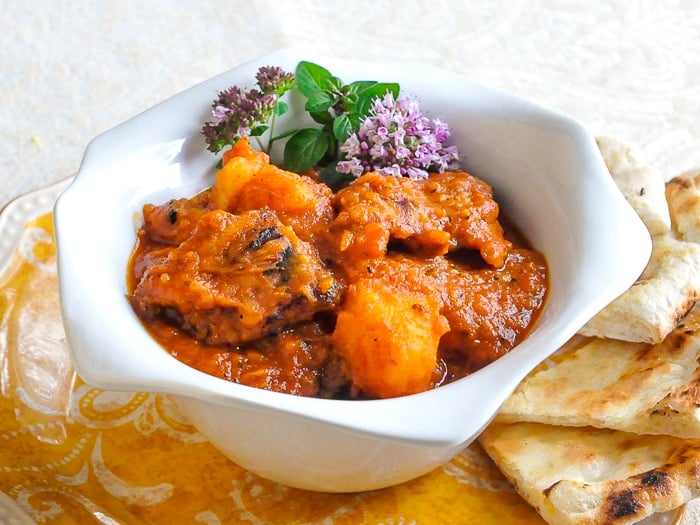 Easy Tomato Potato Chicken Curry in a white bowl with chive flower garnish