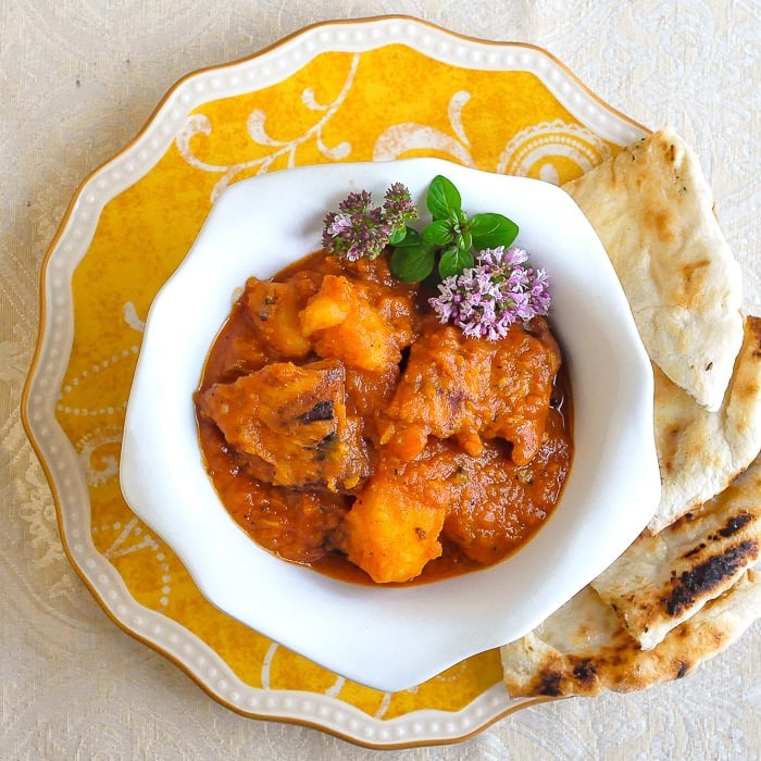 Easy Tomato Potato Chicken Curry overhead shot of curry in a white bowl with naan on the side