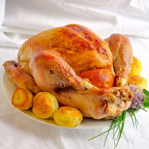 Orange Clove Brined Roast Turkey with roasted potatoes and herbs on a white platter