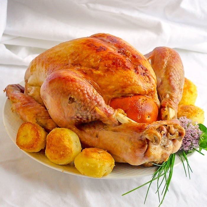 Orange Clove Brined Roast Turkey with roasted potatos and herbs on a white platter