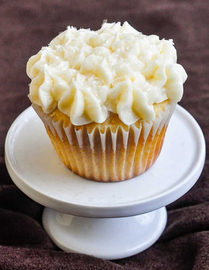 Raspberry Vanilla Cream Cheese Cupcakes on a white pedestal against a brown fabric background