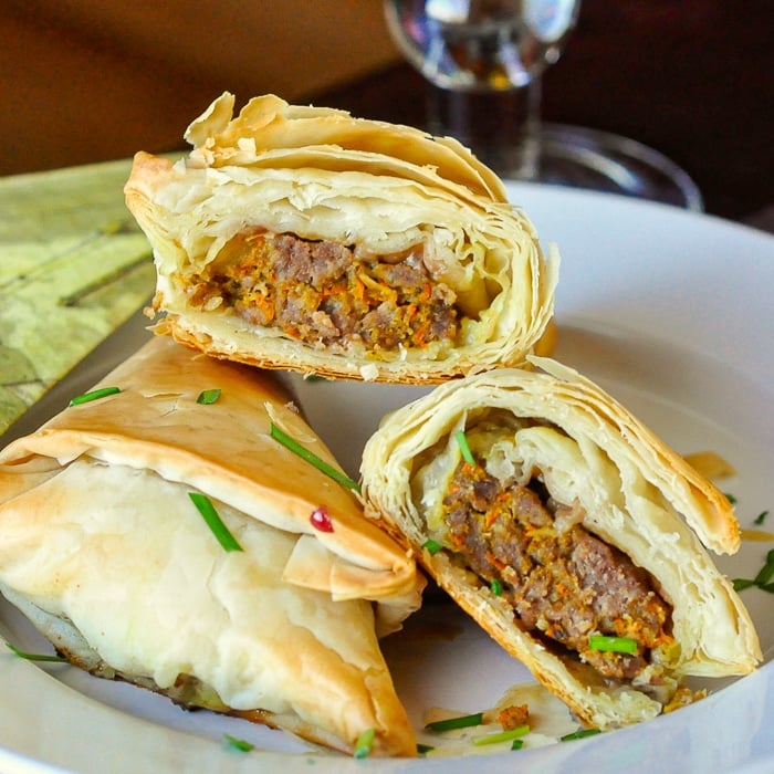 Curry Beef Triangles stacked on a white plate with one cut open to reveal filling