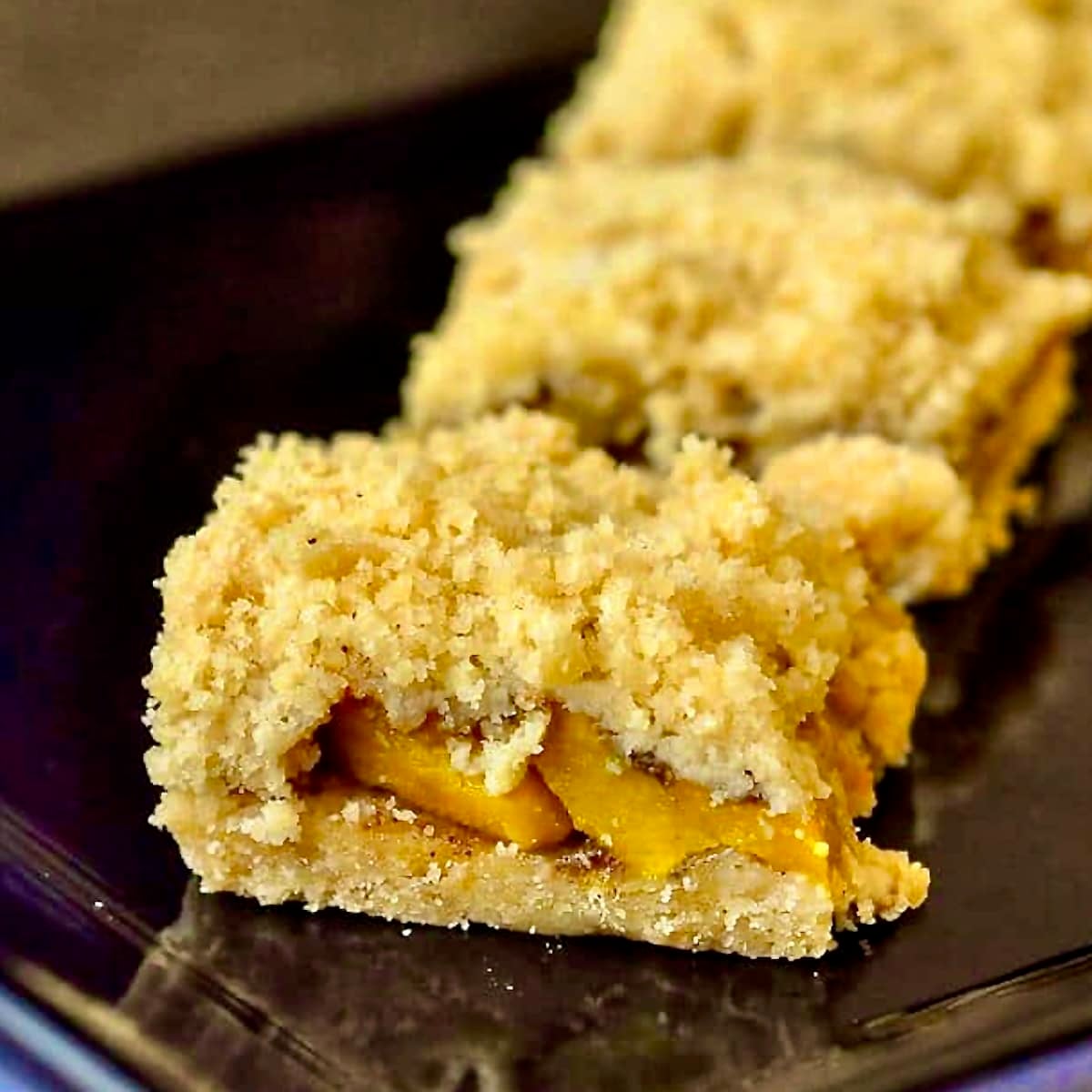 Mango Five Spice Crumble Bars close up photo in a black plate for Google featured image.