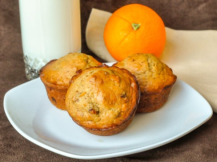 Orange Date Muffins wide shot of 3 muffins on a serving plate with glass of milk and an orange in background