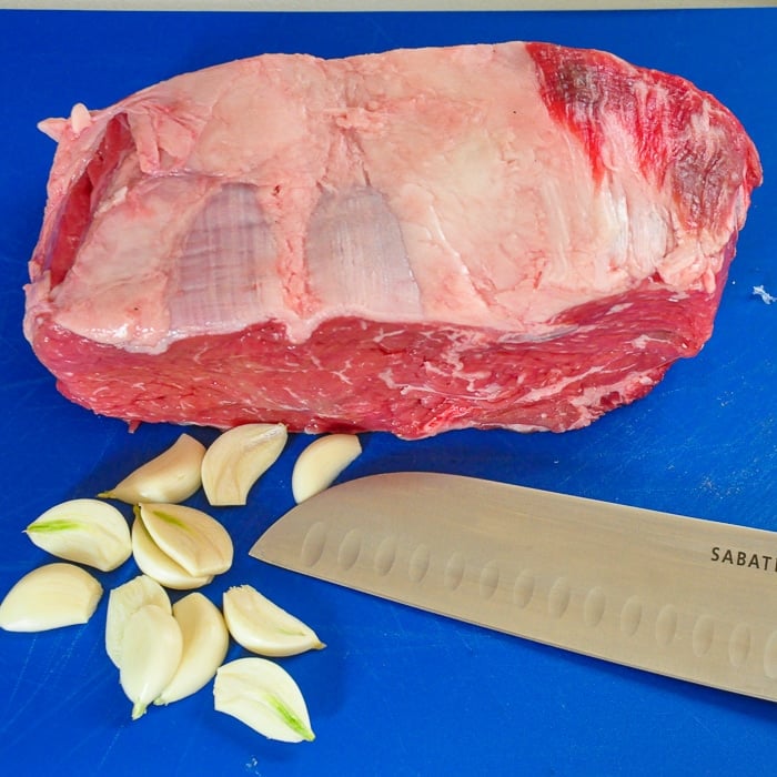 Rib eye Roast with garlic slices on a blue cutting board