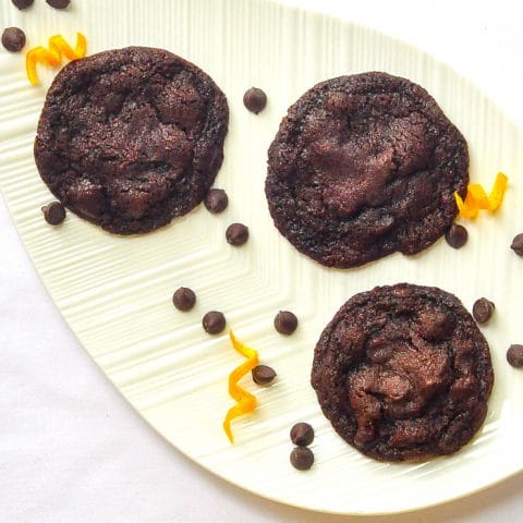 Orange Dark Chocolate Chip Cookies close up overhead phhoto of cookies with orange zest on a white leaf shaped platter.