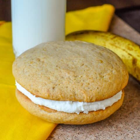 Banana Cream Cheese Whoopie Pies close up photo of a single whoopie pie with milk and banana in background