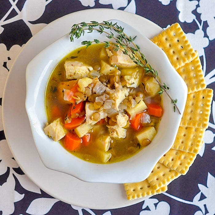 Chicken Thyme and Lentil Soup wide shot image of soup in a white bowl with crackers on the side