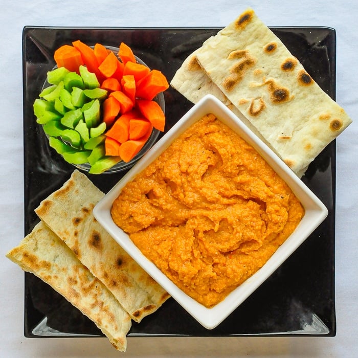 Roasted Red Pepper Hummus in a white bowl with veggies and flatbread